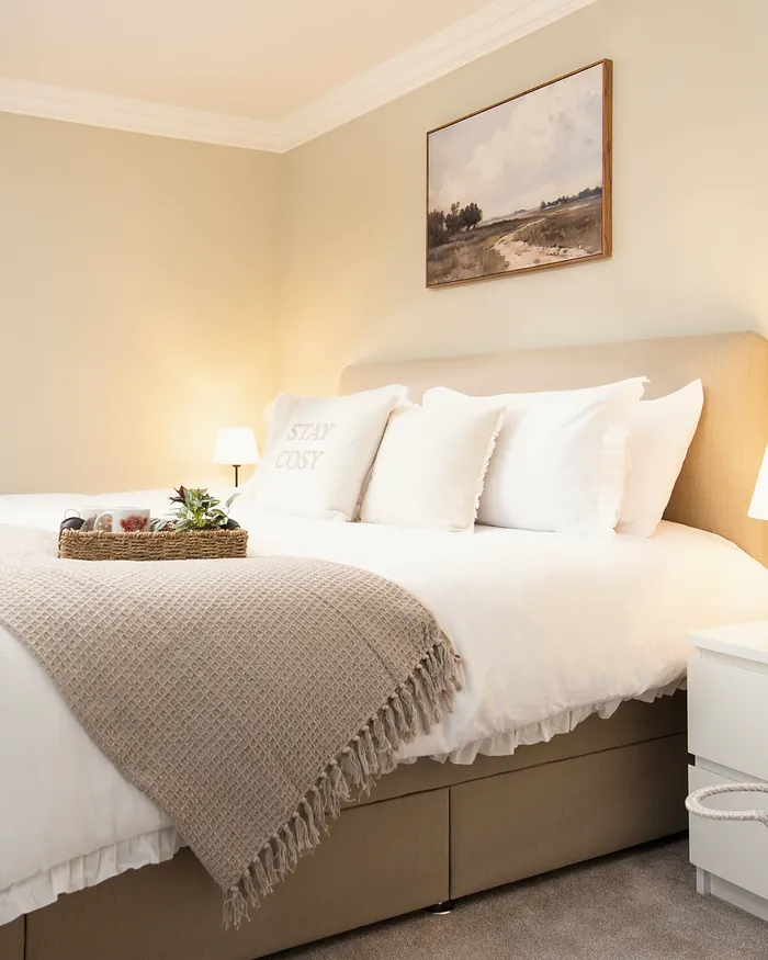 Bedroom with a landscape print above the bed and a knitted throw