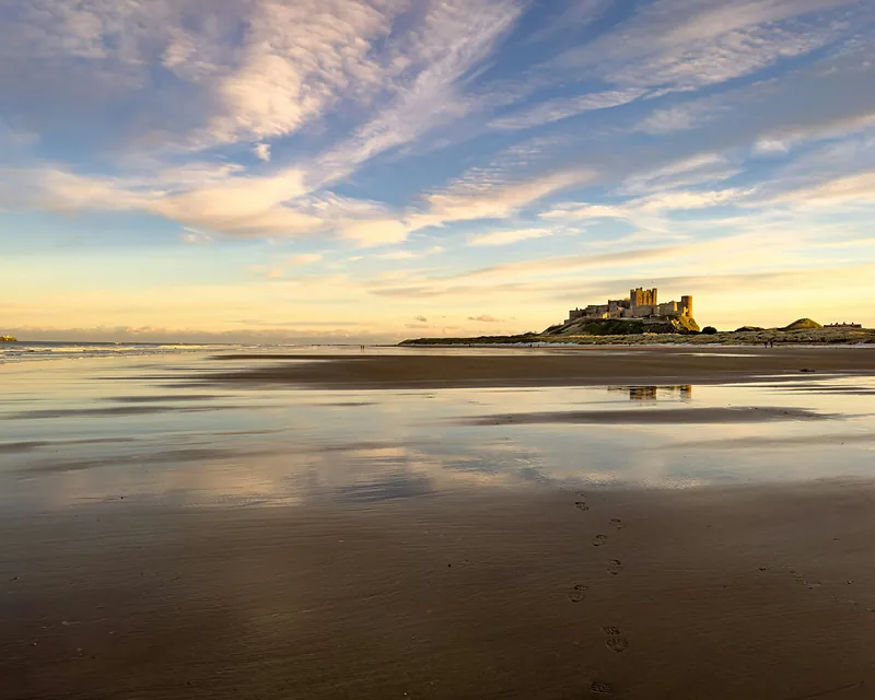 Bamburgh Castle on the horizon at sunset, reflected in the wet sand